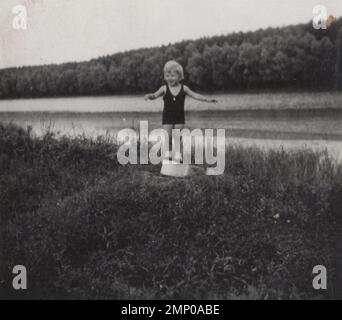 vintage moment / vintage funny moment / vintage photograph / power of the moment / magic moments / little child is playing at the riverside summer time at the 1920s. He/she is standing on the top of the bowl. Stock Photo