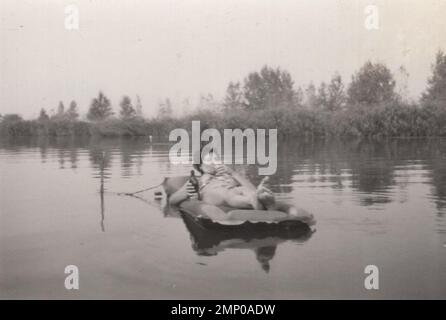 vintage moment / vintage funny moment / vintage photograph / power of the moment / magic moments /enjoy your life photo,lady smoking a cigarette and drinking beer while she is sunbathing and lying Swimming pool Mattress at summer time at 1940s. Stock Photo