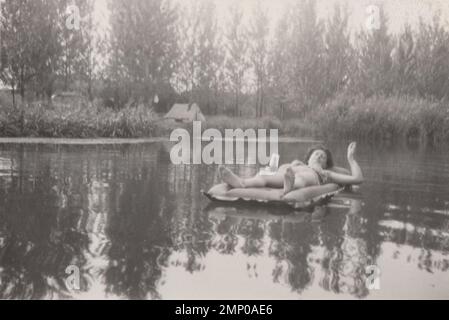 vintage moment / vintage funny moment / vintage photograph / power of the moment / magic moments /enjoy your life photo,lady smoking a cigarette and drinking beer while she is sunbathing and lying Swimming pool Mattress at summer time at 1940s. Stock Photo