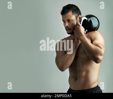 Working hard to reach his fitness goals. Studio shot of a young man working out with a kettle bell against a gray background. Stock Photo