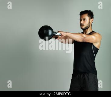 Dedicated to staying in shape. Studio shot of a young man working out with a kettle bell against a gray background. Stock Photo