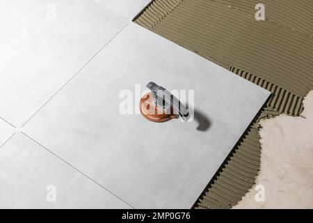 Tiler worker placing or tiling gray ceramic tile in the position over adhesive glue with lash tile leveling system, renovation or recontruction Stock Photo