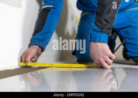 Tiler worker placing or tiling gray ceramic tile in the position over adhesive glue with lash tile leveling system, renovation or recontruction Stock Photo