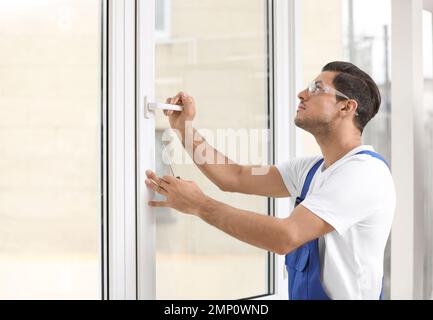 Construction worker repairing plastic window with screwdriver indoors Stock Photo