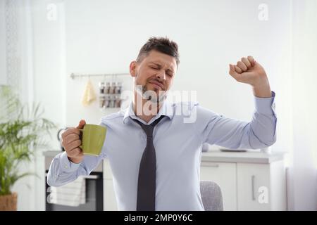 Sleepy man with cup of drink at home in morning Stock Photo