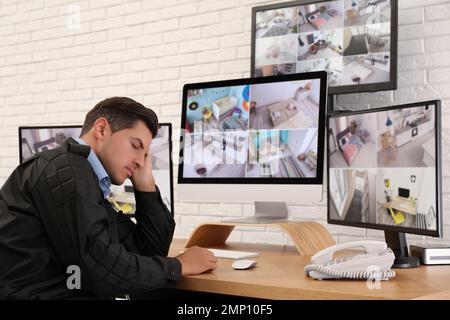 Male security guard sleeping near monitors at workplace Stock Photo