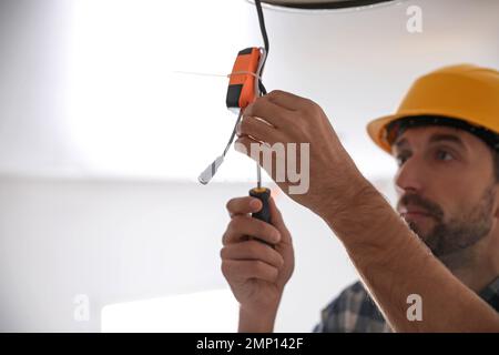 Worker repairing lamp on stretch ceiling indoors. Space for text Stock Photo