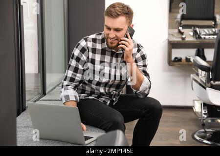 Young business owner talking on phone in his barber shop Stock Photo