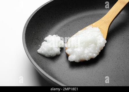 Frying pan with coconut oil and wooden spoon on white background, closeup. Healthy cooking Stock Photo