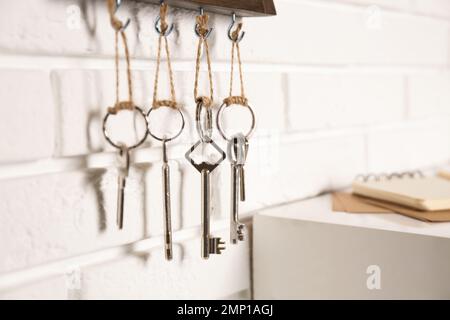 Holder with different keys on white brick wall indoors, closeup Stock Photo