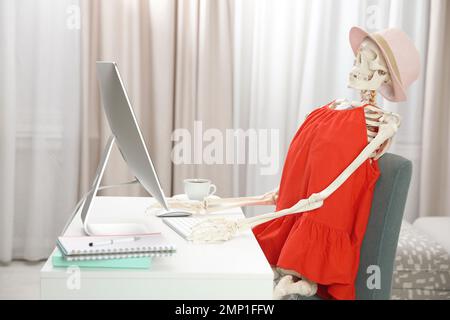 Human skeleton in red dress using computer indoors Stock Photo