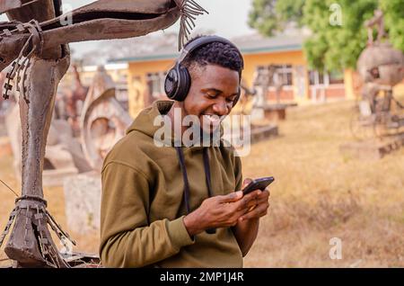 Black young man relaxing outdoors listening to music using phone and headphones. Copy space. Stock Photo