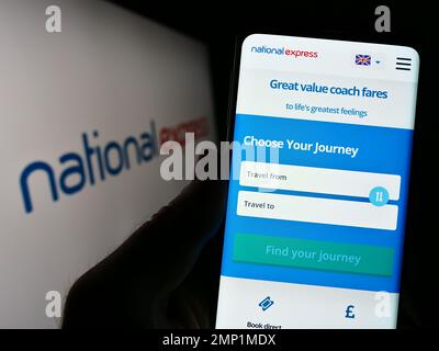 Person holding smartphone with webpage of British company National Express Group plc (NX) on screen with logo. Focus on center of phone display. Stock Photo
