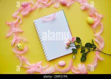 Creative Easter stationery card mock up on yellow background. Decorated Easter with colorful eggs, pink feathers and pink rose. Stock Photo