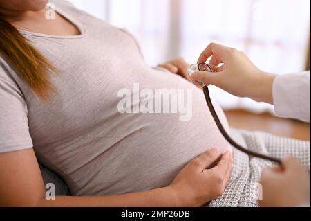 Close-up image of a professional doctor listening baby's heartbeat with a stethoscope, examining pregnant woman in the clinic. Stock Photo