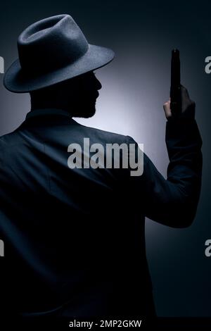 Gangster, silhouette or holding gun on studio background in secret spy, isolated mafia leadership or crime security. Model, man or dark hitman and Stock Photo