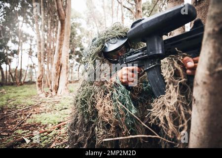 Paintball gun, forrest and man with aim by trees for outdoor war game, strategy or focus in natural camouflage. Shooter, sniper and helmet for safety Stock Photo