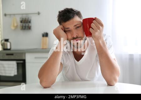 Sleepy man with cup of drink at home in morning Stock Photo