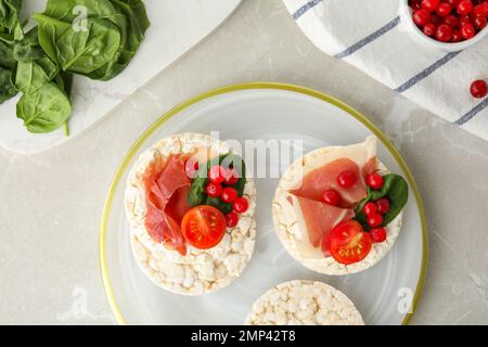 Puffed rice cakes with prosciutto, berries and basil on grey marble table, flat lay Stock Photo