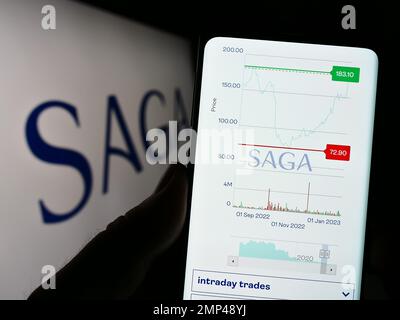 Person holding cellphone with website of travel and financial services company Saga plc on screen with logo. Focus on center of phone display. Stock Photo