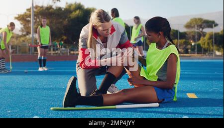 Woman, sports and knee injury in hockey training, practice or game on a blue turf with coach and team. Sport mentor helping female in leg pain Stock Photo