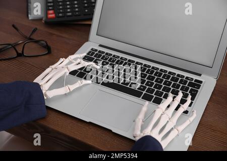 Human skeleton in suit using laptop at table, closeup Stock Photo