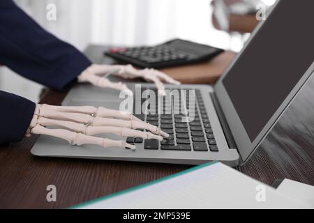 Human skeleton in suit using laptop at table, closeup Stock Photo