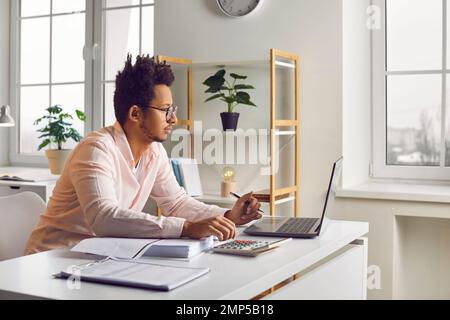 Young indian business man working on laptop at office looking on its screen and making calculations Stock Photo