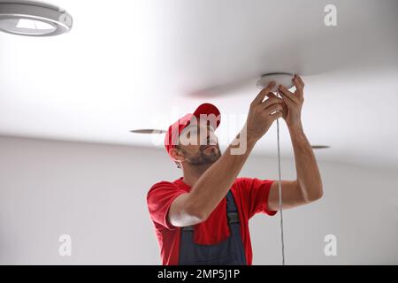 Worker repairing lamp on stretch ceiling indoors Stock Photo