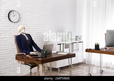 Human skeleton in suit using laptop at table in office Stock Photo