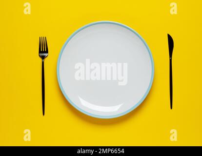 Empty white plate with spoon and fork on yellow background. Meal preparation concept. Stock Photo