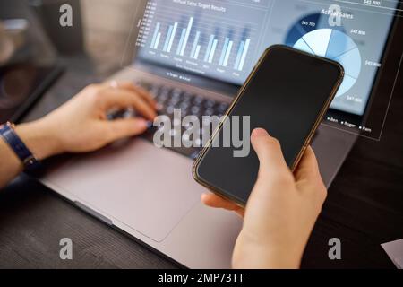 Hands, phone and laptop with hologram in analytics for chart, graph or marketing statistics. Hand of analyst checking 3D digital data for corporate or Stock Photo