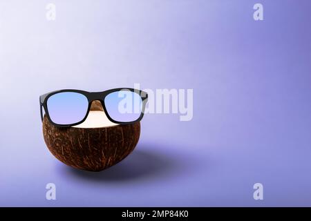 Summer composition on the theme of vacation. Funny coconut with sunglasses on a blue background. Copy space Stock Photo