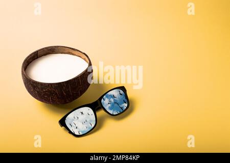 Summer composition on the theme of vacation. Coconut with sunglasses on a yellow background, the color of a sandy beach or a sun. Reflection of birds Stock Photo