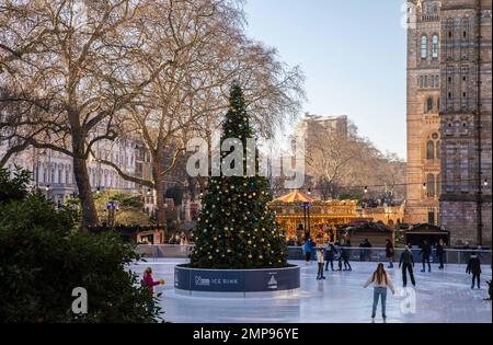 People skating on the ice rink at the Natural History Museum, London in daytime with a Christmas tree in the centre and a carousel in the background. Stock Photo