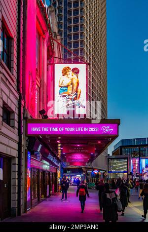Walking along the pavement towards The Dominion Theatre on Tottenham Court Road in London, UK at sunset which is showing Dirty Dancing and lit in pink Stock Photo