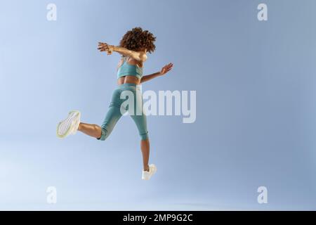Back view of sporty woman running in Mid-Air exercising during cardio workout over studio background Stock Photo