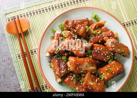 Chinese sweet and sour ribs with green onion and sesame close-up in a plate on the table. Horizontal top view from above Stock Photo