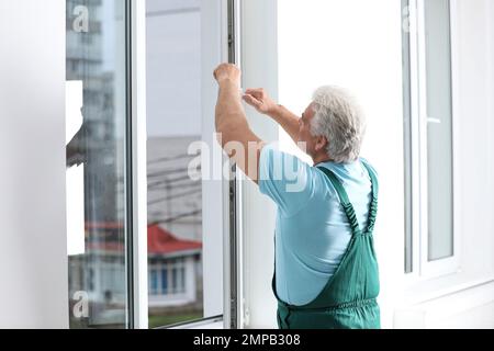 Mature construction worker repairing plastic window indoors Stock Photo