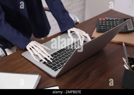 Human skeleton in suit using laptop at table, closeup Stock Photo
