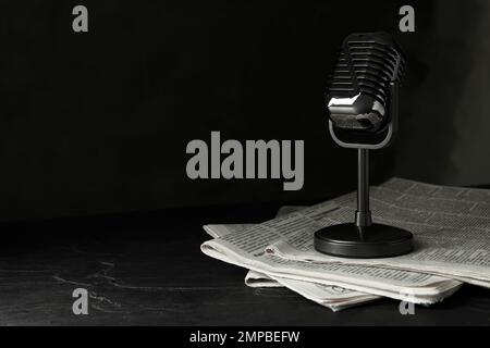 Newspapers and vintage microphone on dark stone table, space for text. Journalist's work Stock Photo