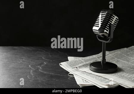 Newspapers and vintage microphone on dark stone table, space for text. Journalist's work Stock Photo