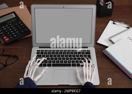 Human skeleton in suit using laptop at table, closeup Stock Photo
