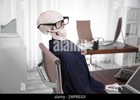 Human skeleton in suit using laptop at table in office Stock Photo