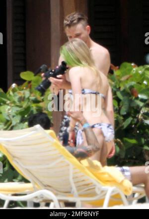 EXCLUSIVE!! Avril Lavigne shows off her fit figure in a black and white bikini during a beach break with her band and her brother, Matt Lavigne, at the Atlantis Paradise Island Resort ahead of her concert. Avril relaxed in a beachside cabana with a group of people including fellow artist Travie McCoy and took a dip in the ocean wearing a hat. Avril, who is still sporting her blonde and green hairstyle following her recent Asian tour, was happy to pose for photos for a member of her group to commemorate the moment over Memorial Weekend. Paradise Island, Bahamas. 5/27/11. Stock Photo