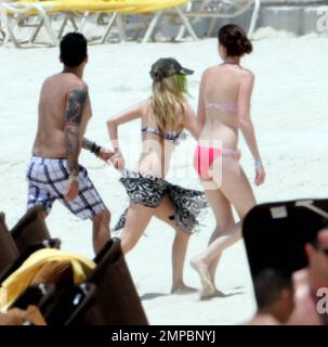 EXCLUSIVE!! Avril Lavigne shows off her fit figure in a black and white bikini during a beach break with her band and her brother, Matt Lavigne, at the Atlantis Paradise Island Resort ahead of her concert. Avril relaxed in a beachside cabana with a group of people including fellow artist Travie McCoy and took a dip in the ocean wearing a hat. Avril, who is still sporting her blonde and green hairstyle following her recent Asian tour, was happy to pose for photos for a member of her group to commemorate the moment over Memorial Weekend. Paradise Island, Bahamas. 5/27/11. Stock Photo