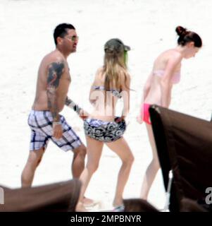 EXCLUSIVE!! Avril Lavigne shows off her fit figure in a black and white bikini during a beach break with her band and her brother, Matt Lavigne, at the Atlantis Paradise Island Resort ahead of her concert. Avril relaxed in a beachside cabana with a group of people including fellow artist Travie McCoy and took a dip in the ocean wearing a hat. Avril, who is still sporting her blonde and green hairstyle following her recent Asian tour, was happy to pose for photos for a member of her group to commemorate the moment over Memorial Weekend. Paradise Island, Bahamas. 5/27/11. Stock Photo