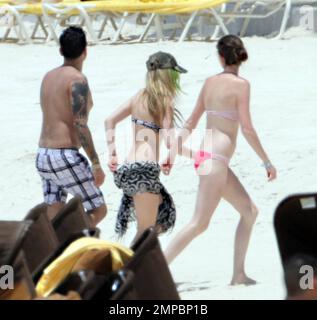 EXCLUSIVE!! Avril Lavigne shows off her fit figure in a black and white bikini during a beach break with her band and her brother, Matt Lavigne, at the Atlantis Paradise Island Resort ahead of her concert. Avril relaxed in a beachside cabana with a group of people including fellow artist Travie McCoy and took a dip in the ocean wearing a hat. Avril, who is still sporting her blonde and green hairstyle following her recent Asian tour, was happy to pose for photos for a member of her group to commemorate the moment over Memorial Weekend. Paradise Island, Bahamas. 5/27/11. Stock Photo