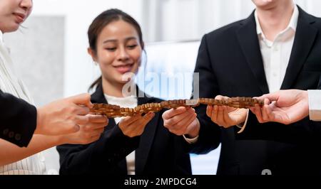 Focus closeup hands holding gears join together in workplace by blur businesspeople in background as concept of harmony in office. Synergy by office Stock Photo