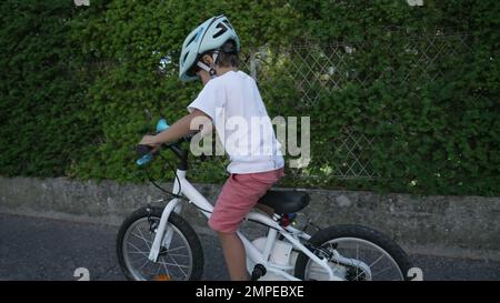 Sportive young boy riding bicycle in city street. Child cyclist rides bike with wheels at urban sidewalk wearing helmet Stock Photo